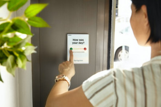 Female employee pressing a green button to give feedback on a device at the office exit door. Credit: Celpax/Unsplash