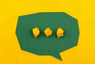 orange sheets of paper lie on a green school board and form a chat bubble with three crumpled papers. Credits: Volodymyr Hryshchenko
