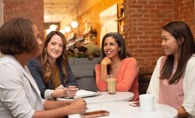Four young ladies indulged in a conversation during coffee break in a workplace canteen