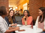 Four young ladies indulged in a conversation during coffee break in a workplace canteen